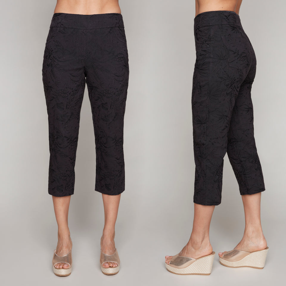 Front and side view of black cropped pants with a subtle floral jacquard texture, worn with wedge sandals.