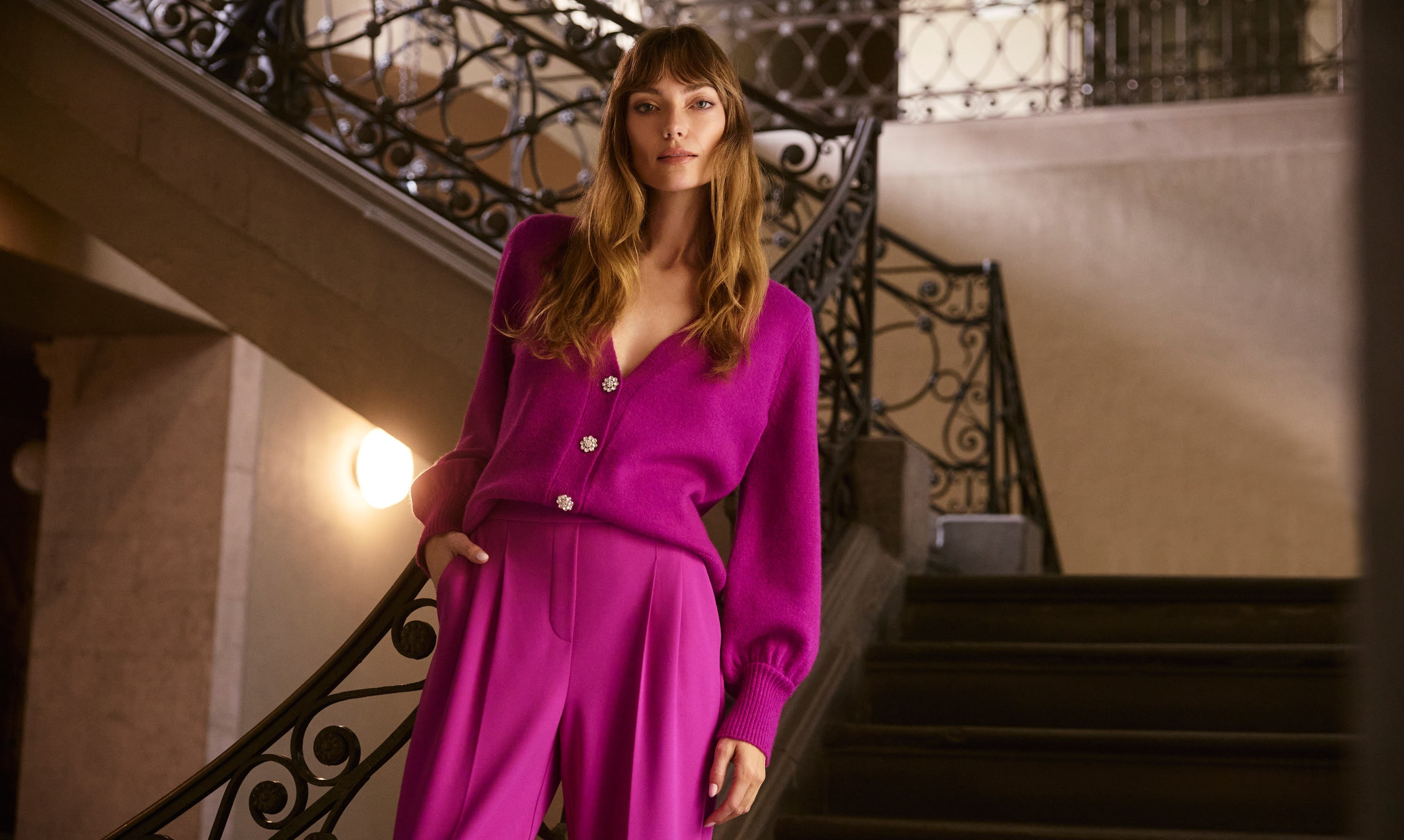 Woman in a bright pink outfit standing on a staircase