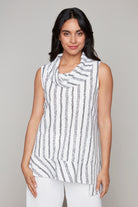 Woman wearing a sleeveless white tunic top with black vertical textured stripes and a draped cowl neckline, styled with white pants.