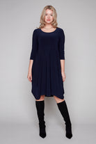 Woman wearing a navy blue dress with long sleeves and black knee-high boots on a gray background