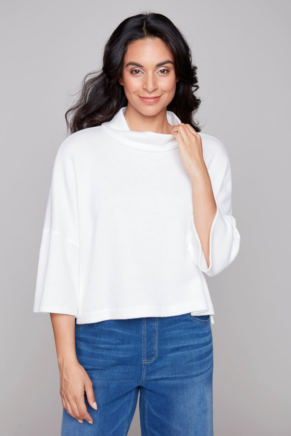 Woman wearing a white top and blue jeans against a gray background