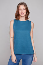 Woman wearing a blue sleeveless top and jeans against a gray background