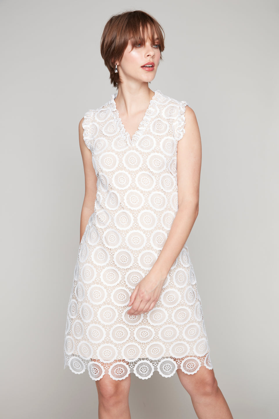 Woman in a white sleeveless dress with circular eyelet embroidery and scalloped hem.