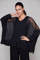 Woman wearing a black outfit with sheer sleeves against a plain background