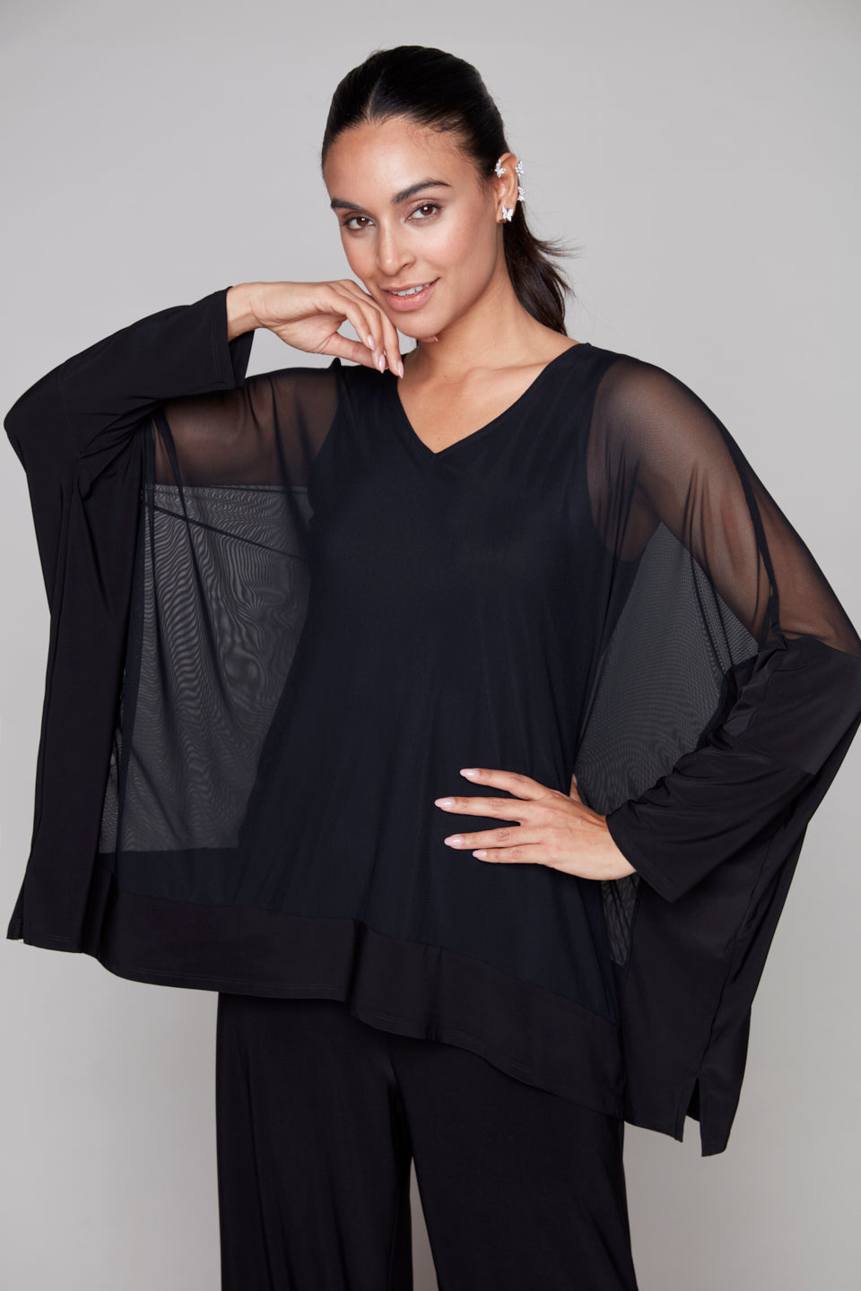 Woman wearing a black outfit with sheer sleeves against a plain background