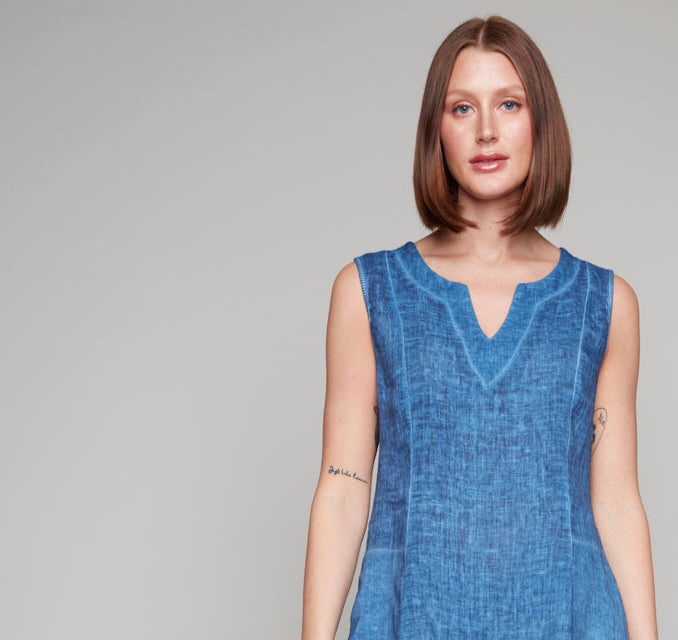 Woman in a sleeveless blue linen dress with notched neckline and sheer hem panel.