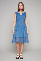 Woman in a sleeveless blue linen dress with notched neckline and sheer hem panel.