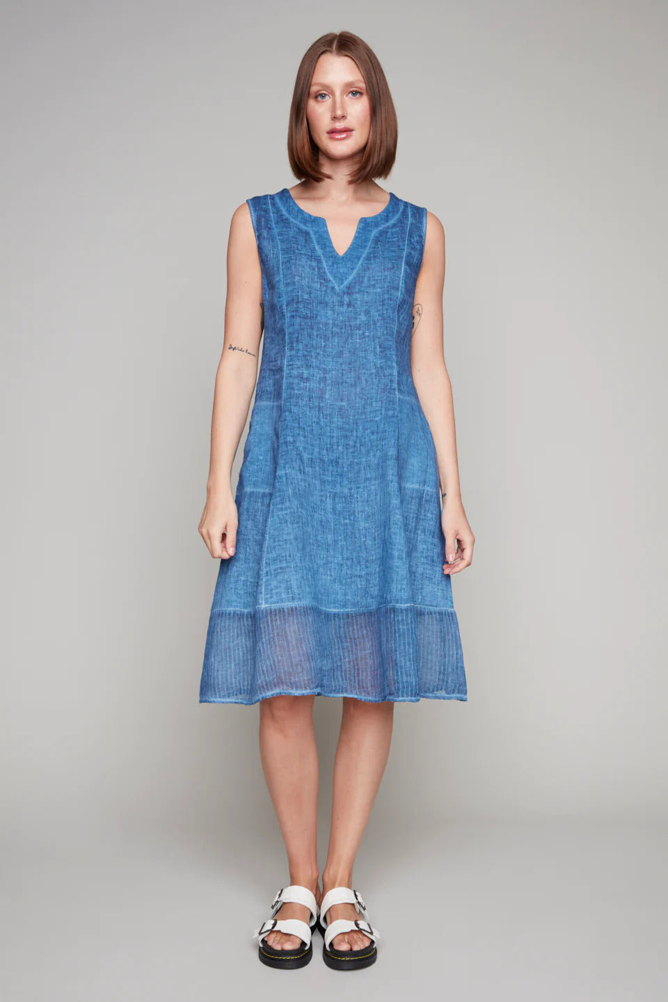Woman in a sleeveless blue linen dress with notched neckline and sheer hem panel.