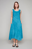 Woman wearing a sleeveless aqua blue midi dress with diagonal pleat detail and asymmetrical hemline.