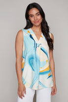 Woman wearing sleeveless top in abstract blue and yellow print with white pants