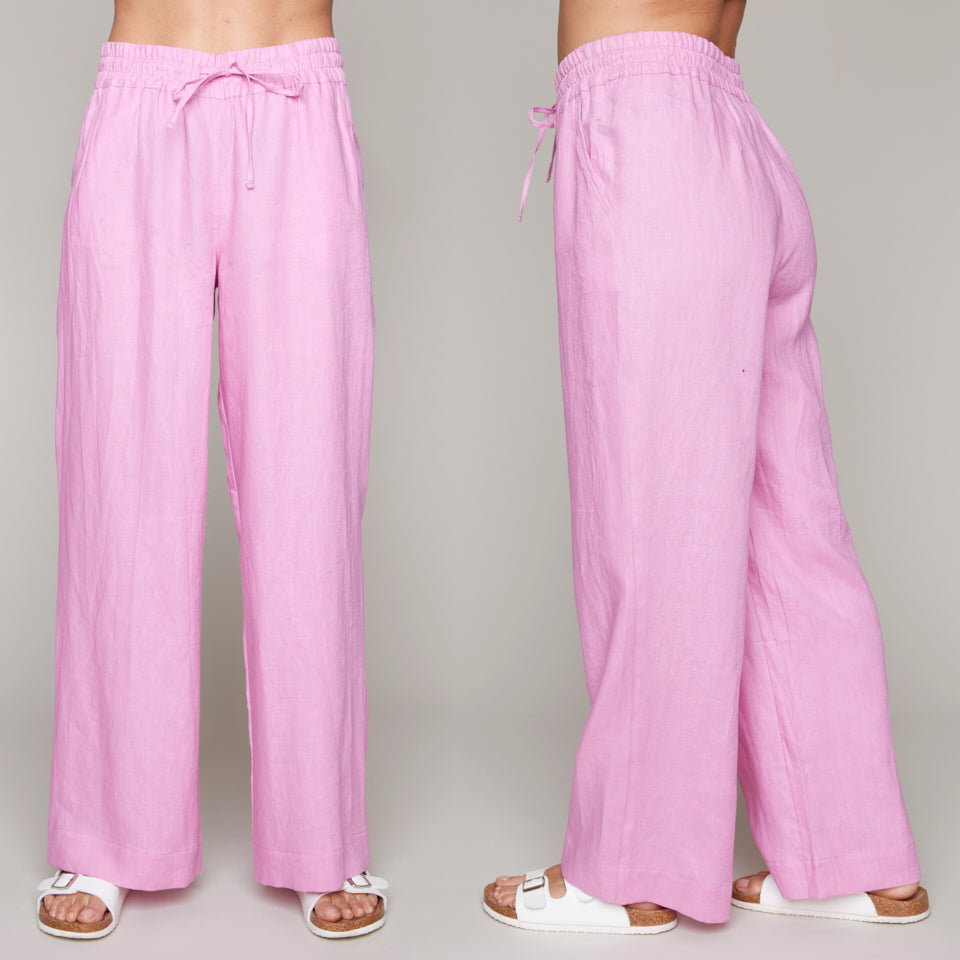 Woman wearing pink wide-leg linen pants with drawstring waist and white sandals