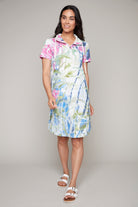 Woman smiling in abstract print short-sleeve dress with floral accents and white sandals