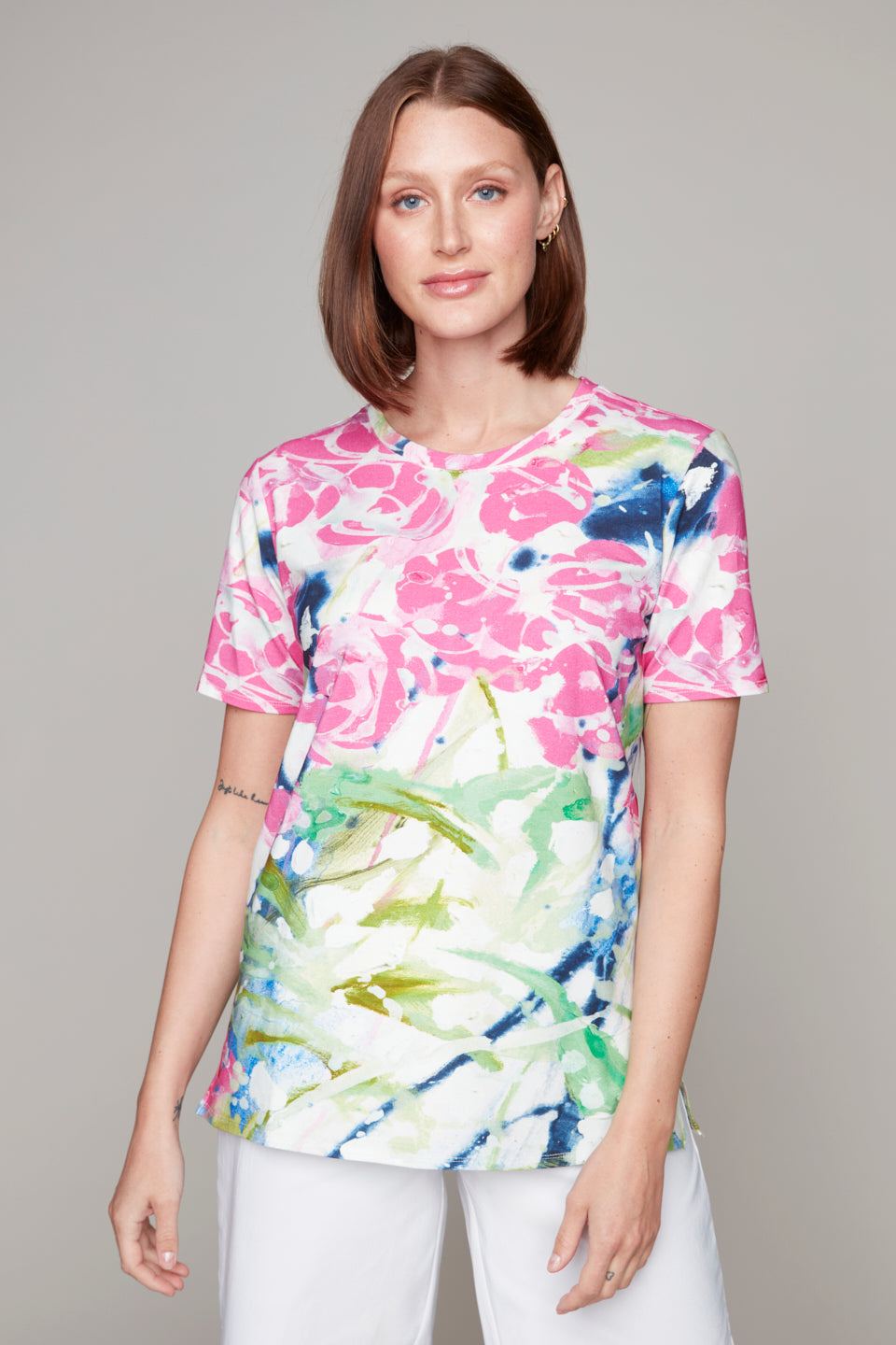 Woman wearing a short sleeve knit tee with a vibrant watercolour floral print in pink, green, blue, and white, paired with white pants.