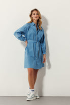 blonde woman standing in blue dress and sneakers