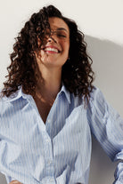 Close-up of a woman smiling with eyes closed, wearing a crisp light blue and white pinstripe blouse with mini navy dot accents.