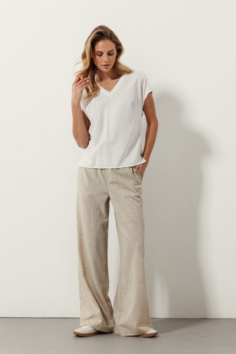 Woman wearing a short sleeve black blouse with grommet detail on the shoulders, paired with light beige wide-leg pants.