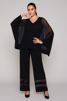 Woman wearing a black outfit with sheer sleeves against a plain background