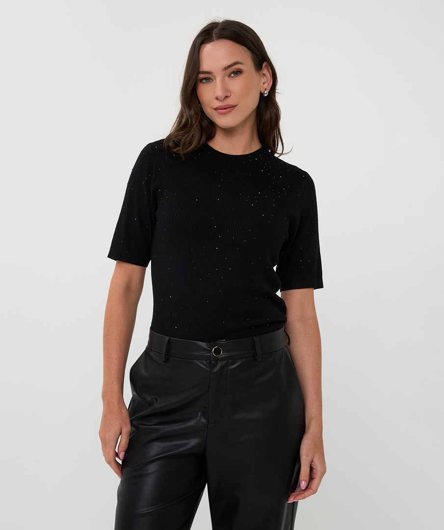 Woman wearing a black short-sleeve top with subtle patterns and black leather pants on a white background