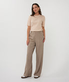 Woman wearing a beige top and brown pants on a white background