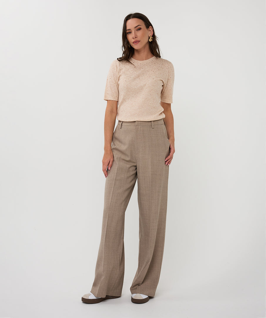 Woman wearing a beige top and brown pants on a white background