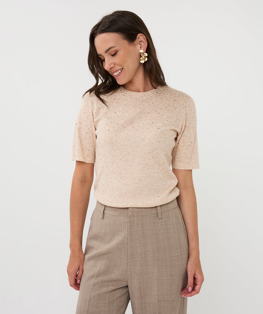 Woman wearing a beige patterned top and beige pants on a white background
