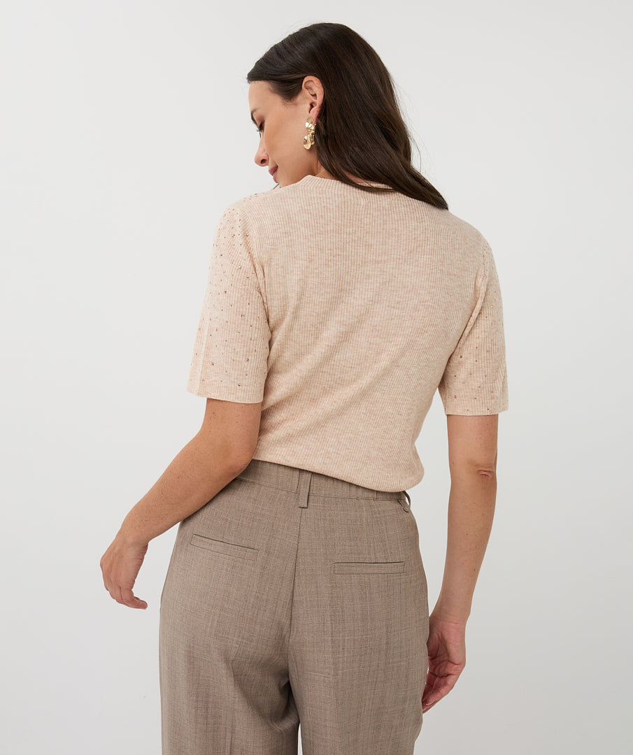 Woman wearing a beige knitted top and brown plaid pants on a white background