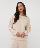 Woman wearing a beige model sweater and pants against a white background