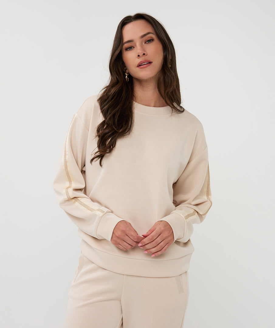 Woman wearing a beige model sweater and pants against a white background