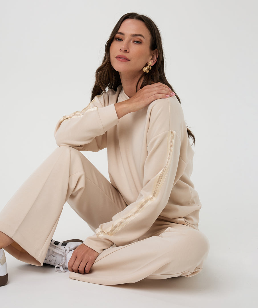 Woman wearing a beige outfit sitting on the floor against a white background