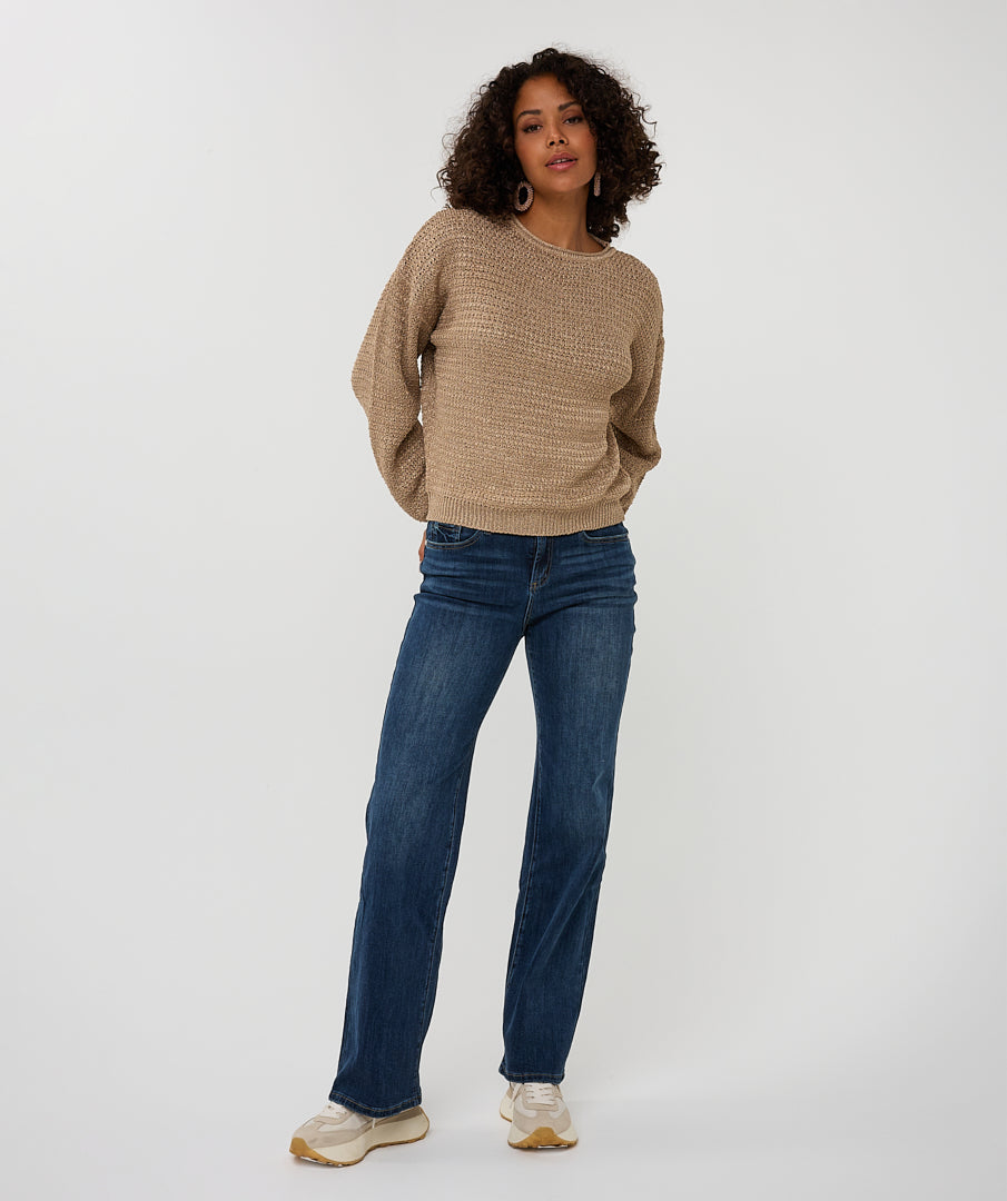 Woman wearing a beige sweater and blue jeans on a white background