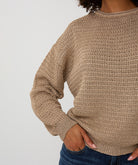 Beige knitted sweater worn by a person on a plain background