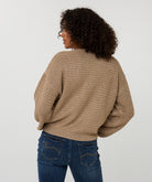 Back View of Person wearing a beige knitted sweater and blue jeans on a white background