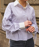 Person wearing a striped shirt with rolled-up sleeves against a stone wall background