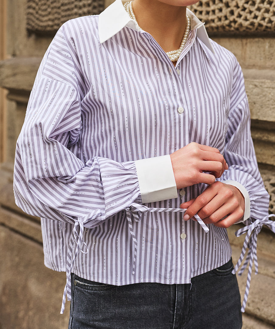 Person wearing a striped shirt with rolled-up sleeves against a stone wall background