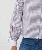 Close-up of a person wearing a striped shirt with rolled-up sleeves and blue jeans on a light gray background