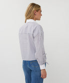 Woman wearing a striped shirt and blue jeans on a plain background side view