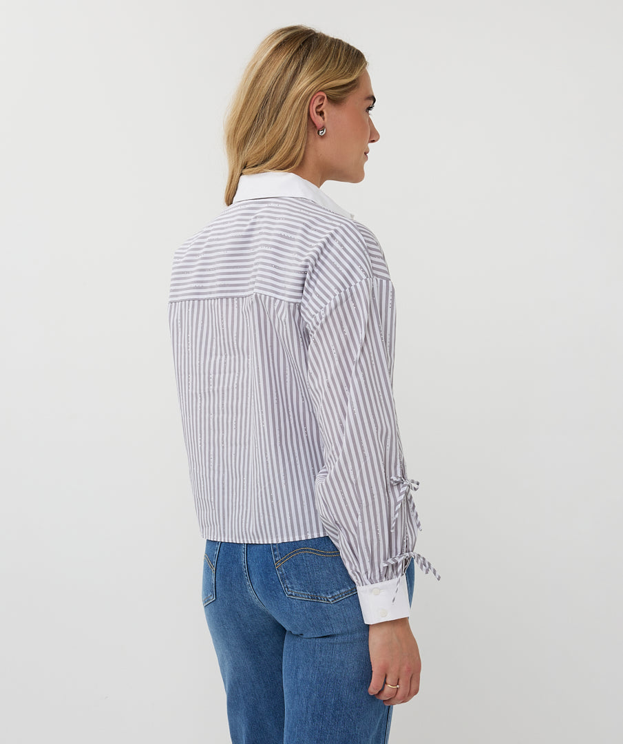 Woman wearing a striped shirt and blue jeans on a plain background side view