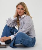 Woman wearing a striped shirt and blue jeans sitting on the floor against a white background