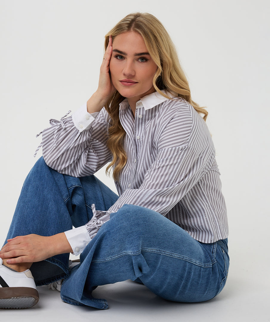 Woman wearing a striped shirt and blue jeans sitting on the floor against a white background