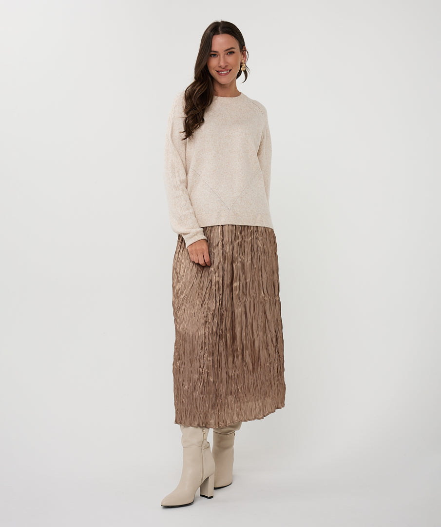 Woman wearing a cream sweater with crinkled skirt on a white background