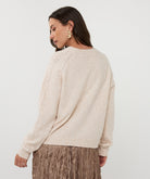Woman wearing a beige sweater and brown pleated skirt on a white background, side back view 