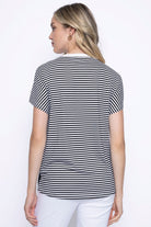 Back view of a woman wearing short sleeve printed top with black and white stripes with a relaxed fit, paired with white pants.