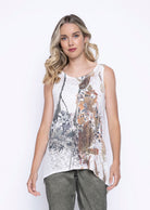 Woman wearing a white sleeveless top with an abstract floral and sequin-embellished design in muted earthy colors, styled with sage green pants.
