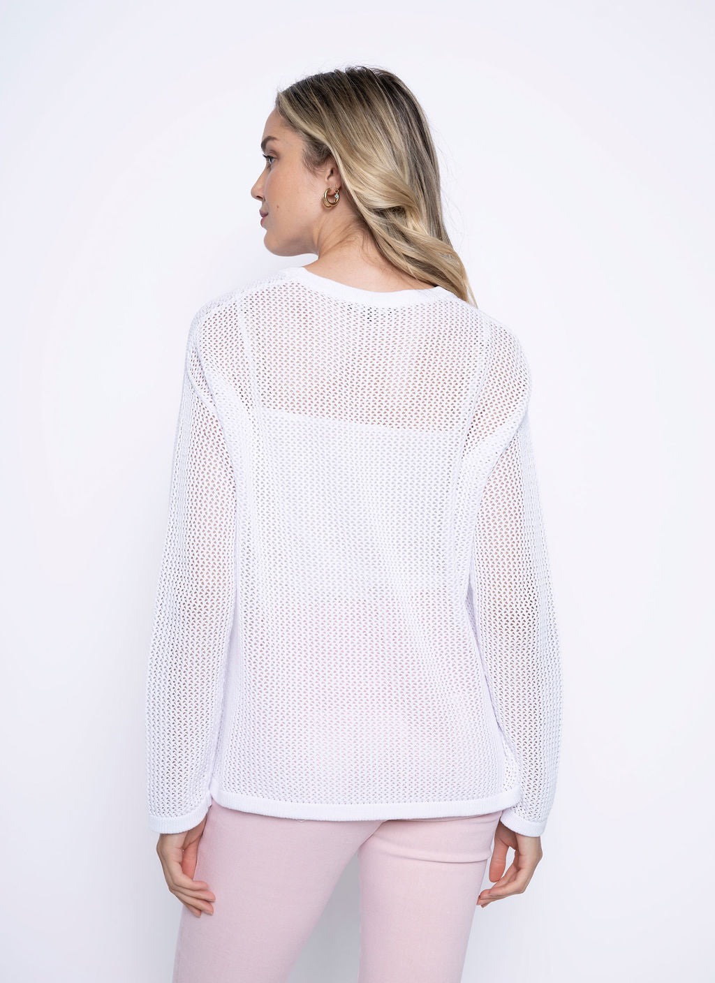 Back view of a woman wearing a long sleeve white mesh cotton top, showing the sheer texture and relaxed fit.