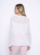 Back view of a woman wearing a long sleeve white mesh cotton top, showing the sheer texture and relaxed fit.