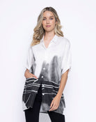 Woman wearing an oversized white button-up shirt with black dip-dye effect and abstract lines, styled with black pants.