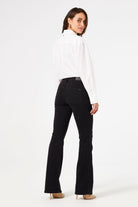 Model wearing black bootcut jeans and a white blouse, shown from the back in a neutral pose.