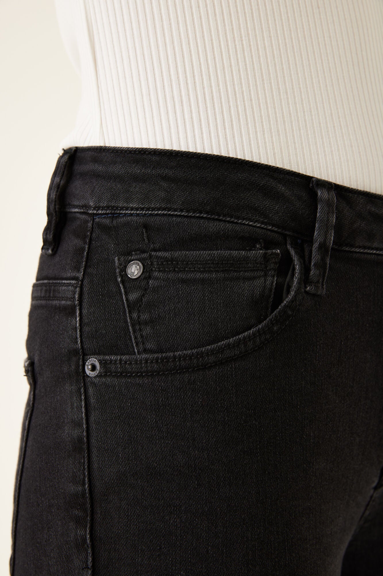 Detailed view of the front pocket and coin pocket on black jeans, highlighting stitching and rivet hardware.
