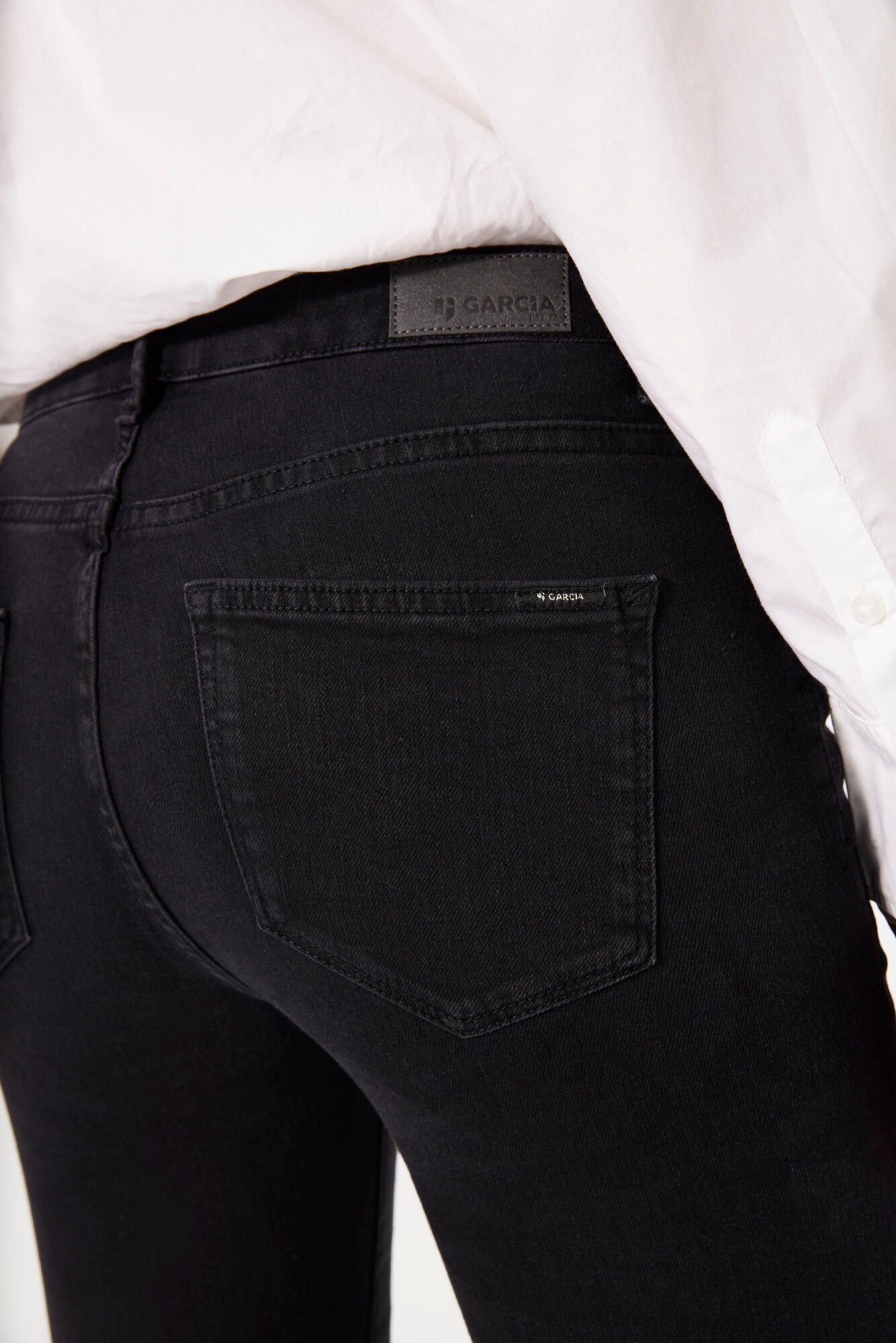 Close-up of black denim showing the back pocket, leather logo patch, and waistband seam detail.