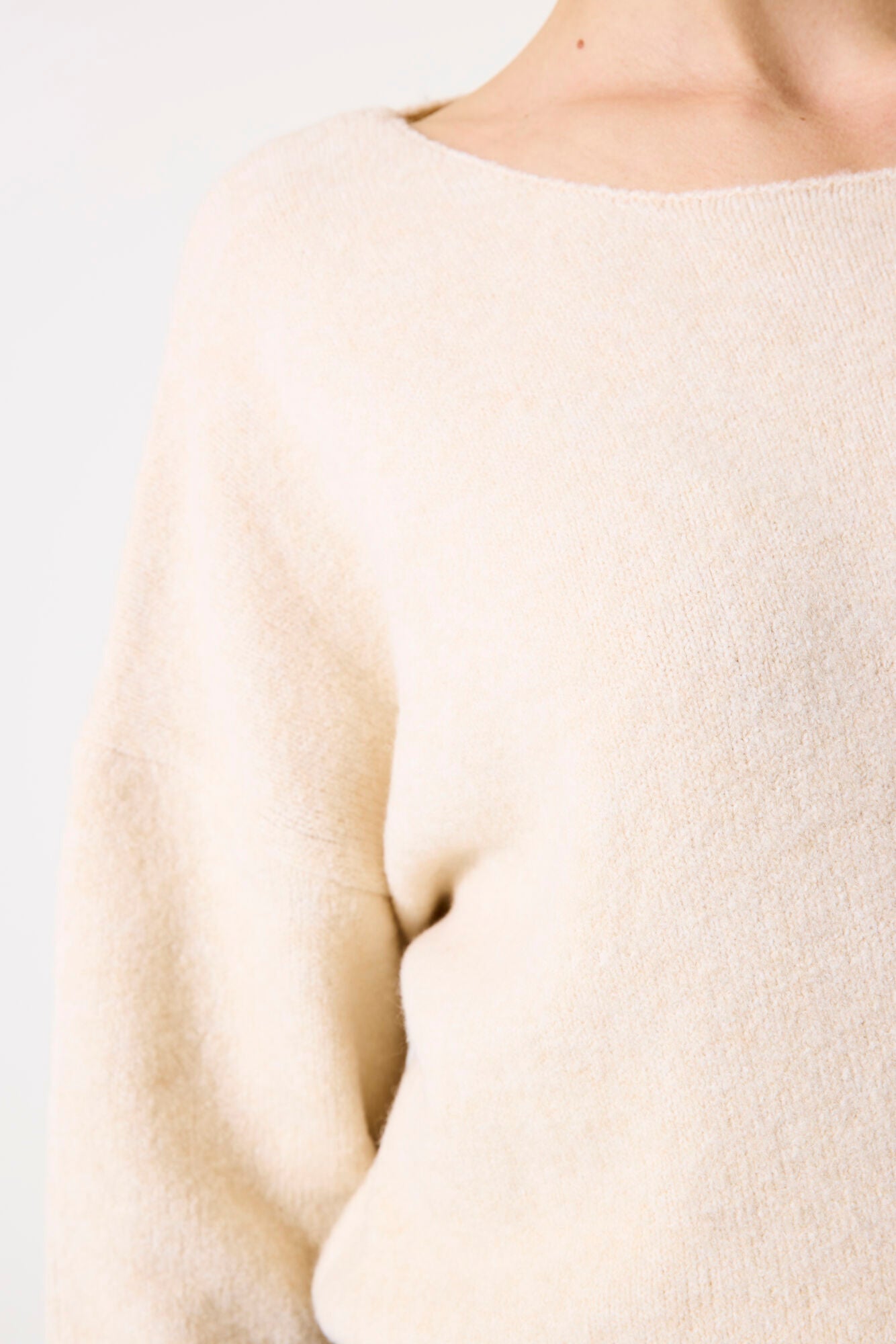 Close-up of the soft knit texture and neckline of the beige sweater.